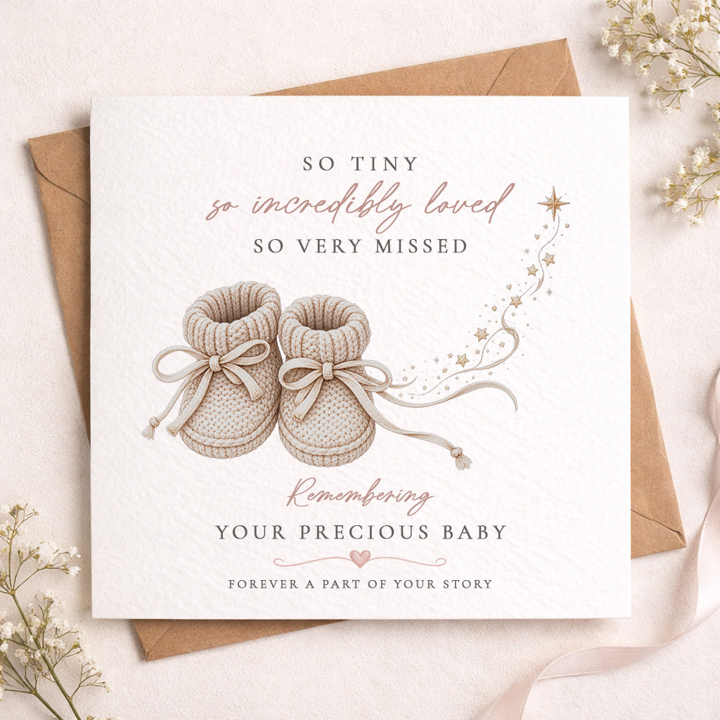 A square baby remembrance card with a kraft envelope, styled on a light beige surface with dried flowers. The card features an illustration of baby booties and elegant text reading 'SO TINY so incredibly loved SO VERY MISSED' and 'Remembering YOUR PRECIOUS BABY FOREVER A PART OF YOUR STORY'.