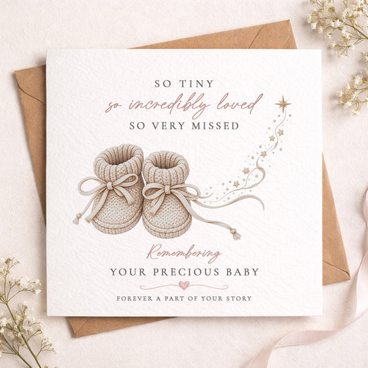 A square baby remembrance card with a kraft envelope, styled on a light beige surface with dried flowers. The card features an illustration of baby booties and elegant text reading 'SO TINY so incredibly loved SO VERY MISSED' and 'Remembering YOUR PRECIOUS BABY FOREVER A PART OF YOUR STORY'.