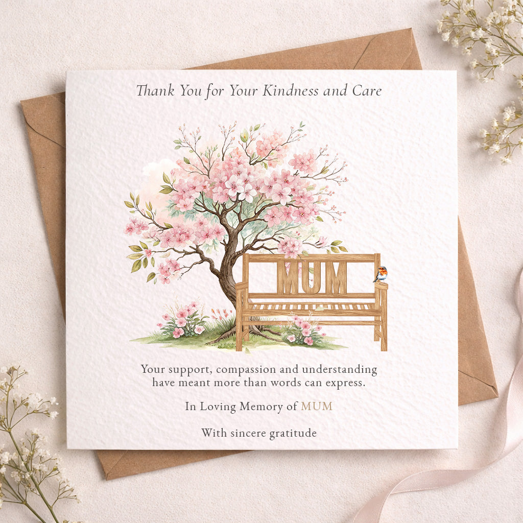 A square memorial thank-you card with a watercolor illustration of a blossom tree and a wooden bench with the word “MUM” on it, placed on top of a brown envelope. The card reads, “Thank You for Your Kindness and Care” and includes a message of remembrance.