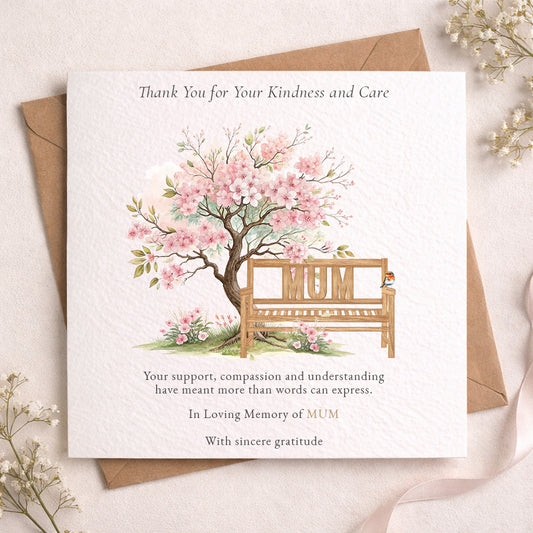 A square memorial thank-you card with a watercolor illustration of a blossom tree and a wooden bench with the word “MUM” on it, placed on top of a brown envelope. The card reads, “Thank You for Your Kindness and Care” and includes a message of remembrance.
