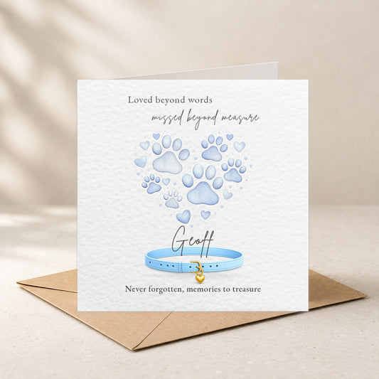 A square white memorial card with a kraft envelope behind it, featuring blue paw prints and a blue collar illustration with the text 'Loved beyond words missed beyond measure' and 'Never forgotten, memories to treasure.' The card is shown standing upright on a light beige surface with soft shadow overlays.