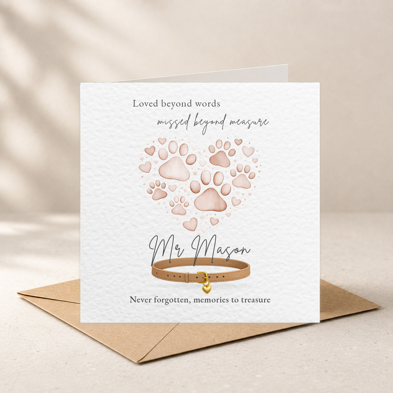 A square white memorial card with a kraft envelope behind it, featuring paw prints arranged in a heart shape, a tan dog collar illustration, and personalized text reading 'Loved beyond words', 'missed beyond measure', 'Mr. Mason', and 'Never forgotten, memories to treasure'.