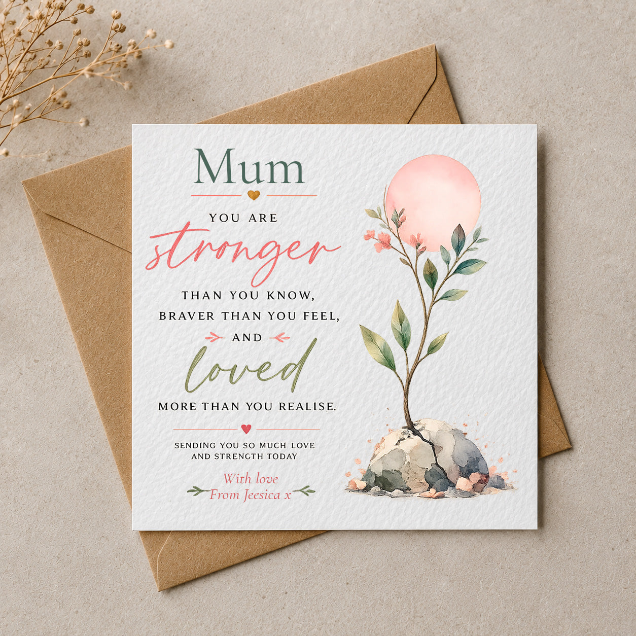 A square white greeting card with a watercolor floral design and sentimental text for 'Mum', placed on top of a brown kraft envelope on a neutral beige surface with dried flowers in the corner.