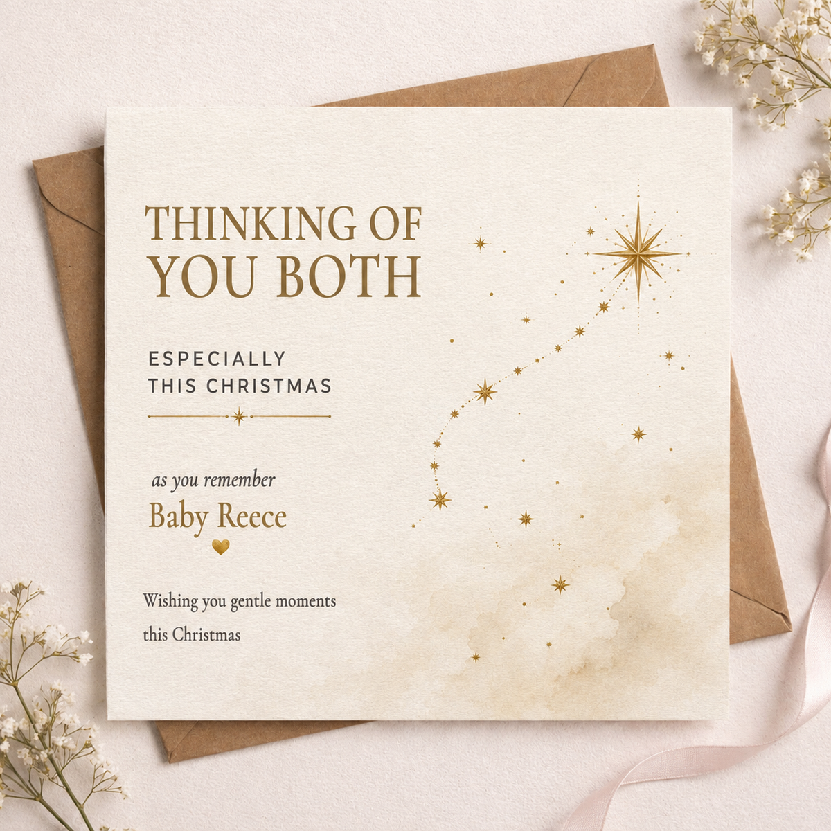 A square Christmas greeting card with a warm cream background and gold text reading 'THINKING OF YOU BOTH' and 'ESPECIALLY THIS CHRISTMAS' for 'Baby Reece', styled on top of brown envelopes with dried flowers and a pale pink ribbon.