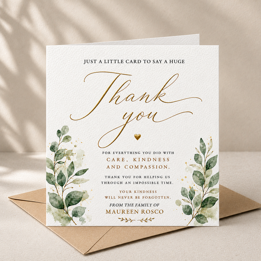 A square thank-you card with elegant gold script and green watercolor eucalyptus leaves, shown standing on top of a kraft envelope against a warm beige background with soft leaf shadows.
