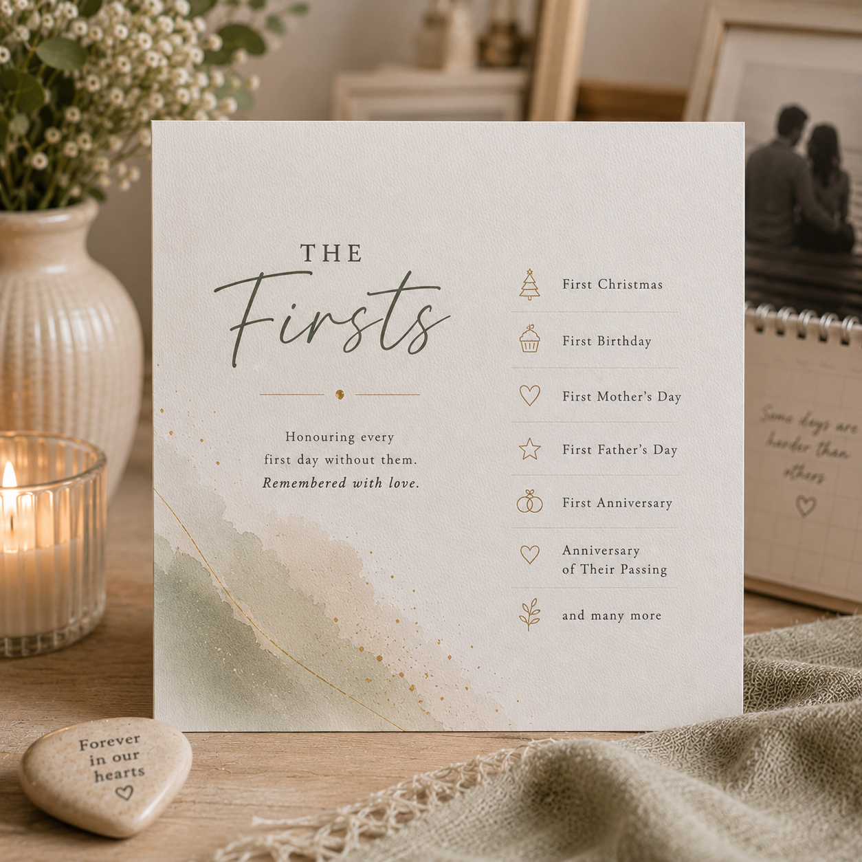 A square white keepsake card titled 'THE Firsts' with gold text and small gold icons listing milestones, displayed on a wooden surface with a candle, flowers, and fabric in a styled indoor setting.