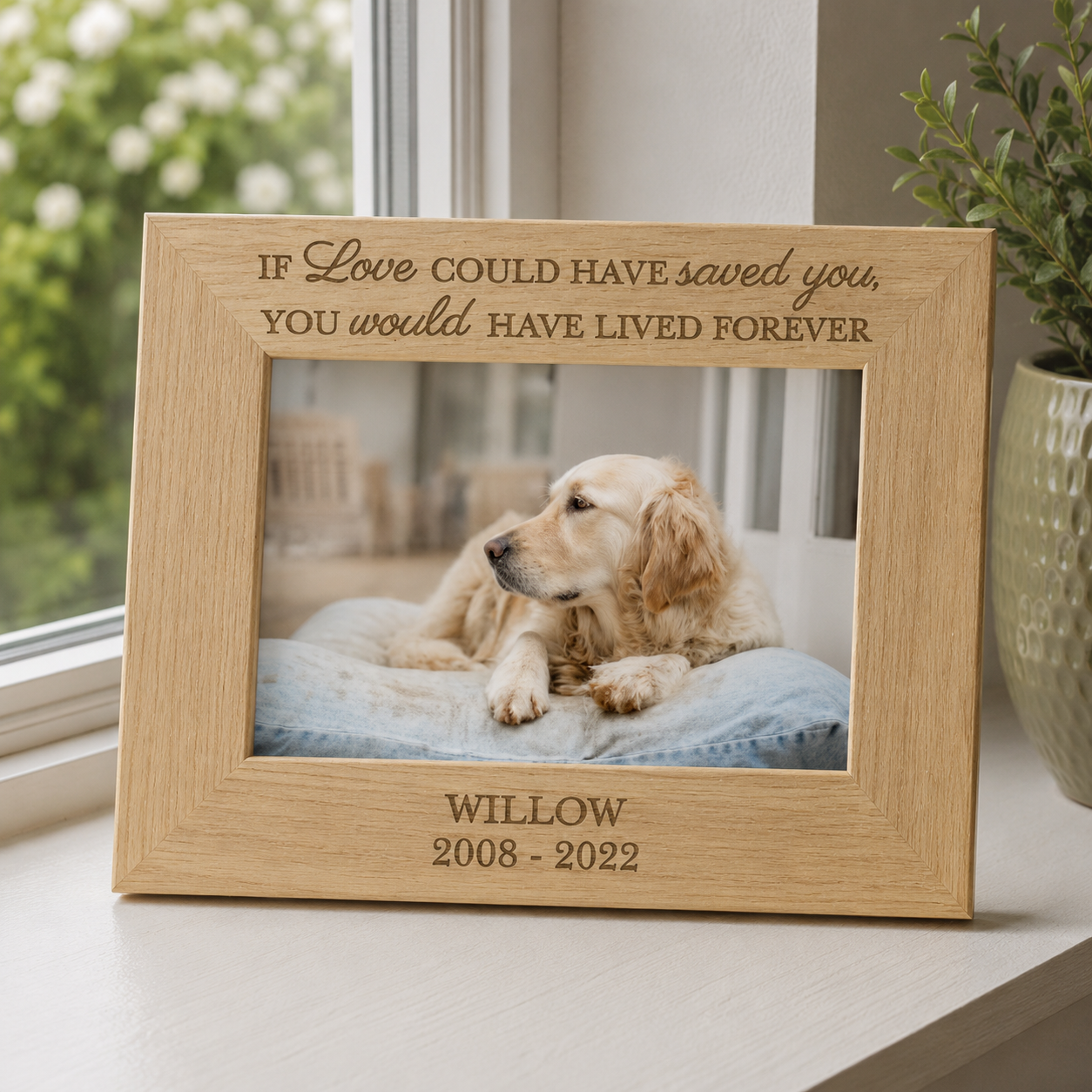 A personalized wooden photo frame with engraved text, displayed on a windowsill. The frame contains a photo of a golden retriever dog on a blue cushion.