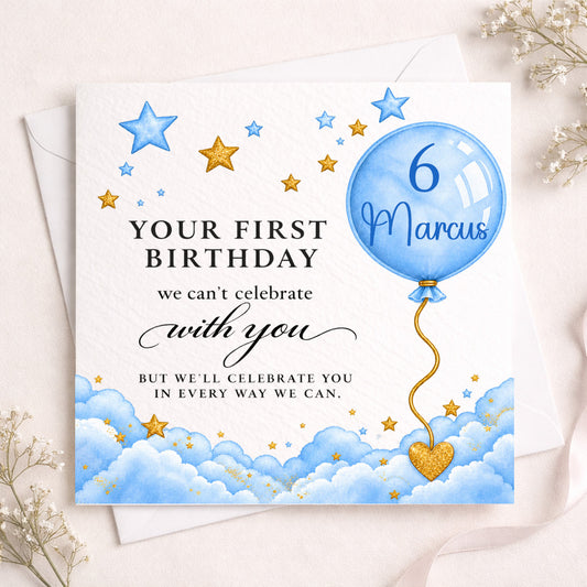 A personalized first birthday card for a boy named Marcus, featuring a blue balloon with '6 Marcus' and a gold heart, set against a background of blue clouds and gold stars. The card is styled on a white envelope with dried flowers on a light beige surface.