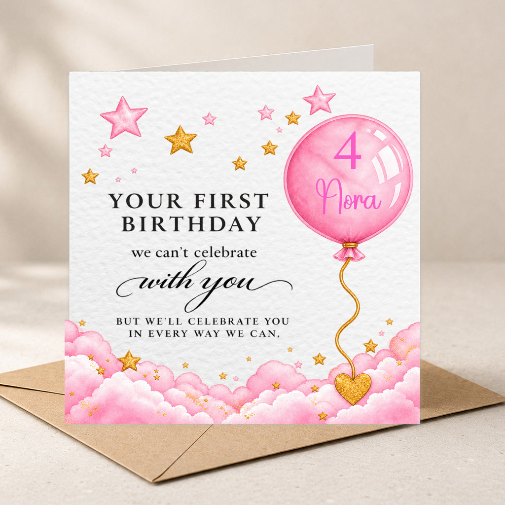 A square birthday card with a pink and gold watercolor design, shown standing on top of a brown envelope against a soft beige background. The card reads 'YOUR FIRST BIRTHDAY we can't celebrate with you BUT WE'LL CELEBRATE YOU IN EVERY WAY WE CAN.