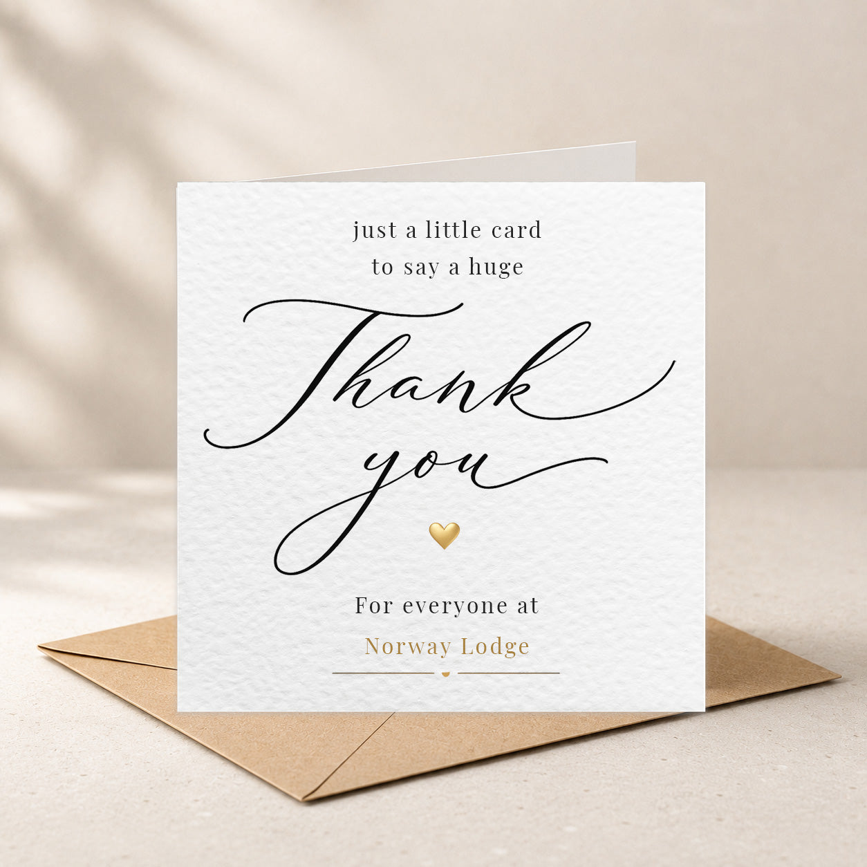 A white textured thank-you card with elegant black script and gold accents, displayed upright on a brown kraft envelope against a warm beige background with soft shadow overlays.