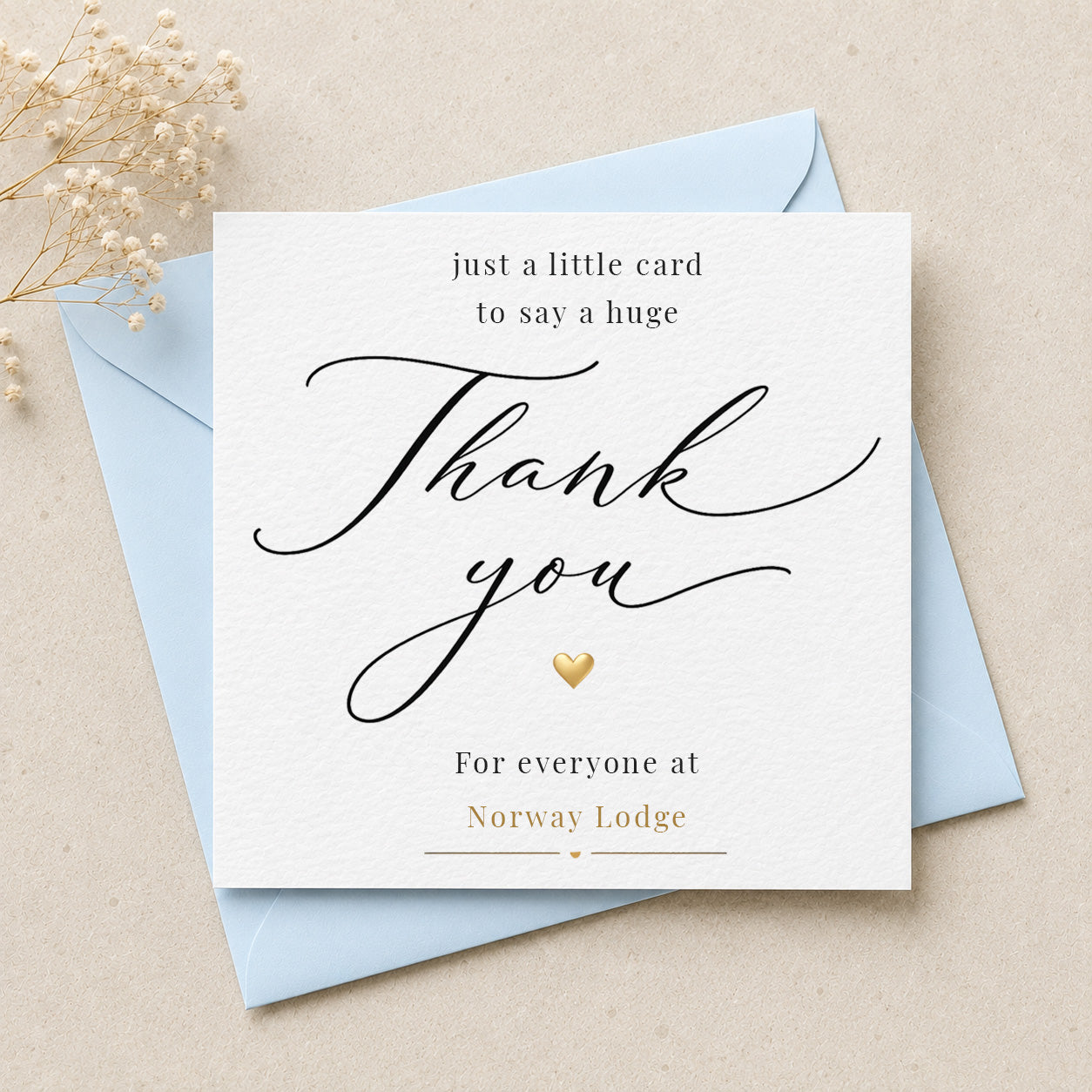 A square white thank-you card with elegant black script and small gold text, layered over light blue envelopes on a beige surface with dried flowers in the corner.