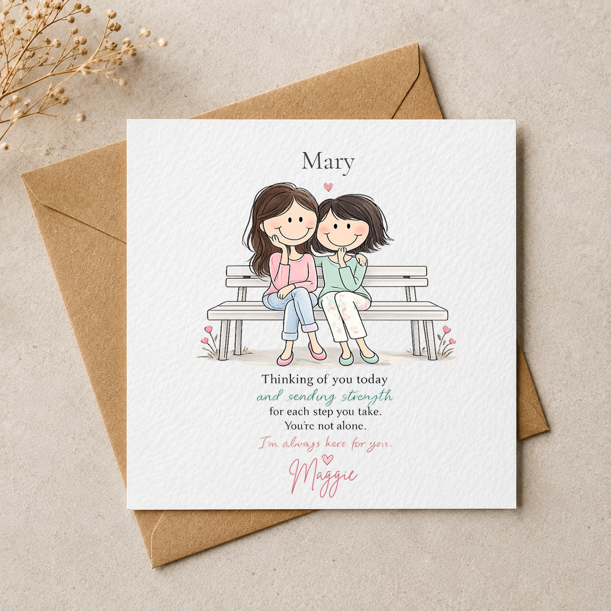A square white greeting card with a cute cartoon illustration of two girls sitting on a bench, placed on top of a brown kraft envelope. The card has the name 'Mary' at the top and a sentimental message printed below, with 'Maggie' written in pink script at the bottom.