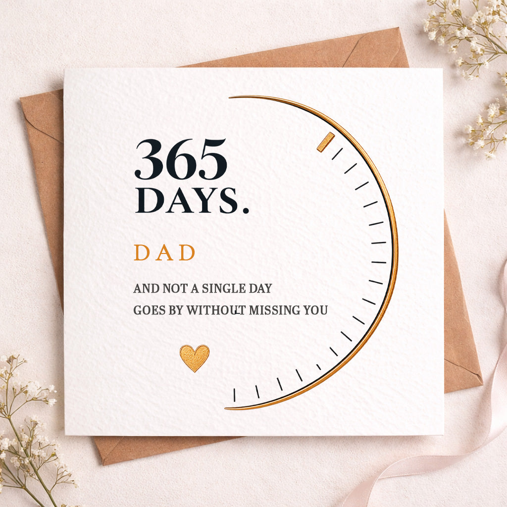 A square white greeting card with a gold and black arc graphic and the text '365 DAYS. DAD AND NOT A SINGLE DAY GOES BY WITHOUT MISSING YOU,' styled on top of brown envelopes with small white flowers on a light beige surface.