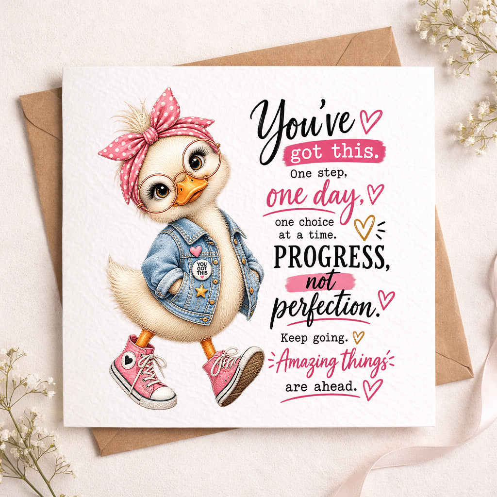 A square greeting card featuring a cute cartoon duck wearing a pink polka-dot bow, denim jacket, and pink sneakers, next to motivational text. The card is displayed on top of a brown kraft envelope with small white flowers in the corners on a light beige surface.