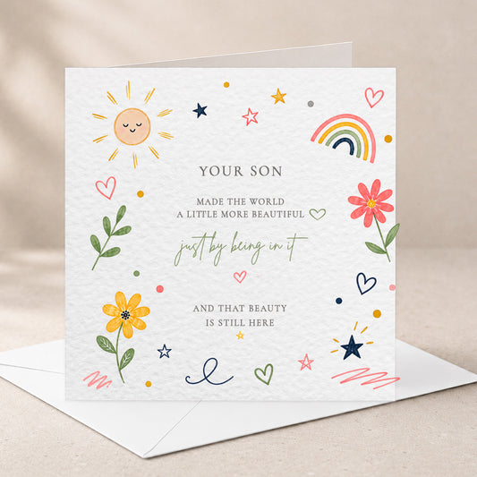 A square white greeting card with a textured paper finish, decorated with colorful hand-drawn illustrations including a smiling sun, flowers, stars, hearts, and a rainbow. The center contains personalized text reading 'YOUR SON MADE THE WORLD A LITTLE MORE BEAUTIFUL just by being in it AND THAT BEAUTY IS STILL HERE.