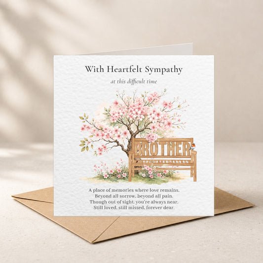 A square sympathy greeting card with a kraft envelope, featuring a watercolor illustration of a cherry blossom tree and bench with the word 'BROTHER' on the seat, photographed on a warm beige surface.
