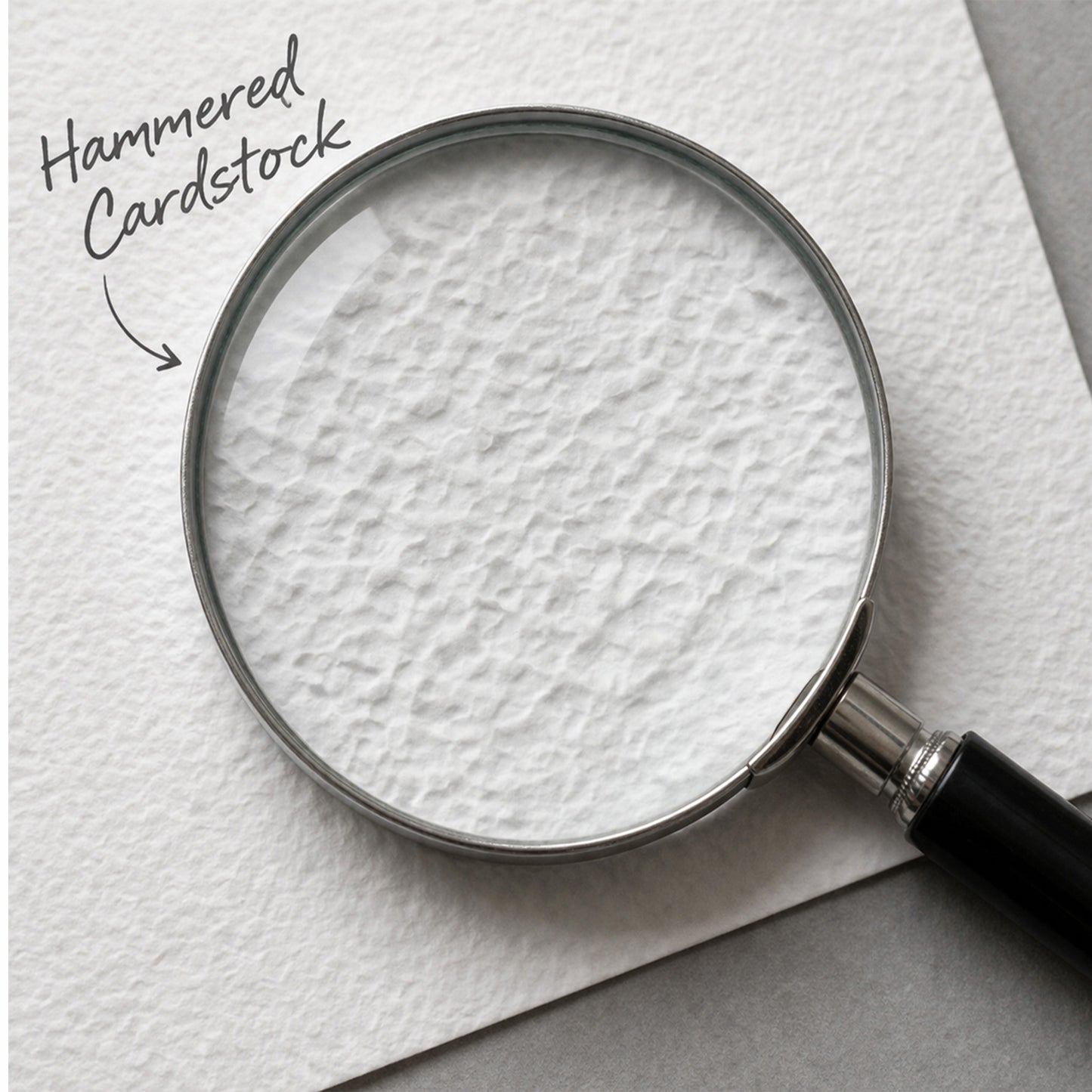 A close-up of a magnifying glass showing the texture of white hammered cardstock, with handwritten text reading 'Hammered Cardstock' and an arrow pointing to the surface.