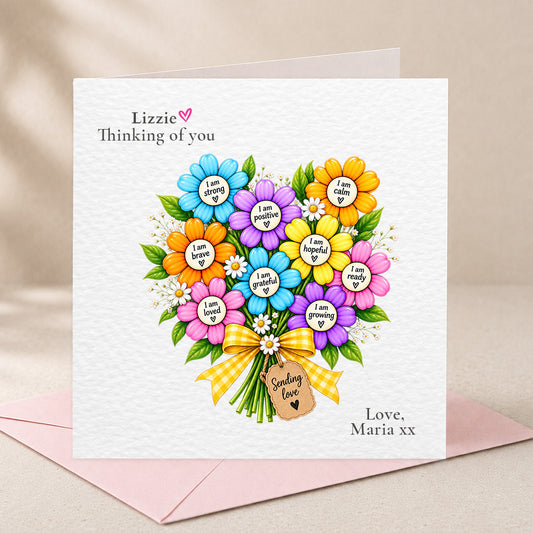 A square white greeting card with a colorful flower bouquet illustration and personalized text reading 'Lizzie Thinking of you' and 'Love, Maria xx', shown with a pink envelope on a soft beige background.