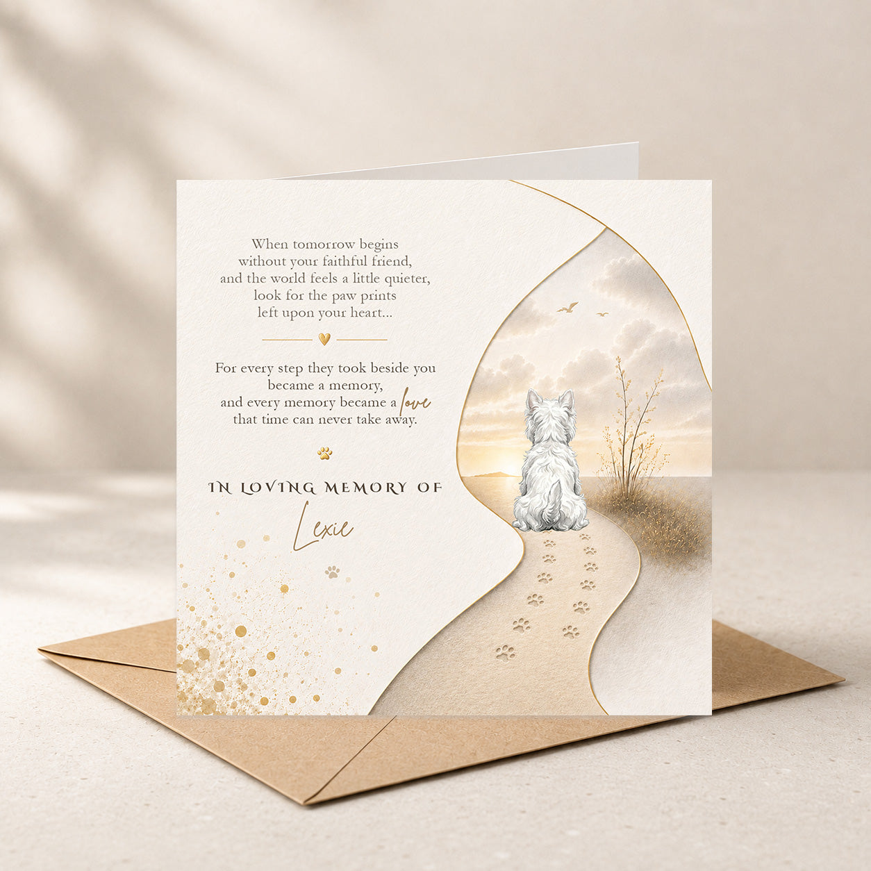 A pet memorial card with a soft beige and cream design, featuring a small white cat sitting on a path with paw prints, placed on top of a brown envelope against a warm neutral background.