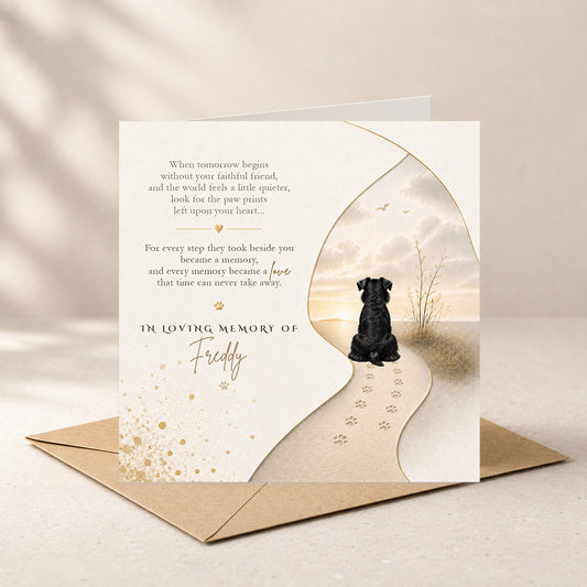 A pet memorial card with a black dog silhouette and paw prints, displayed on a brown envelope against a warm beige background.