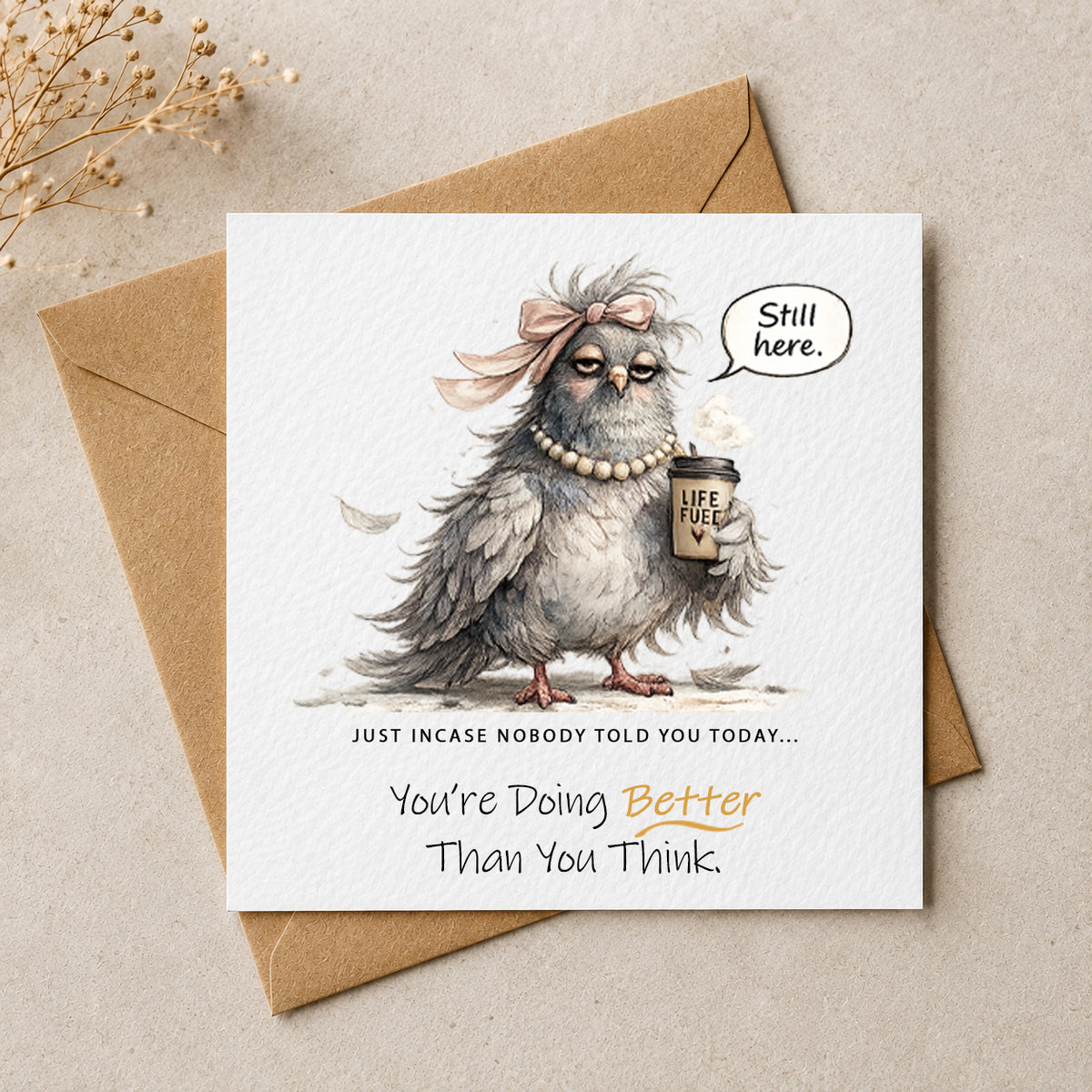 A square greeting card with a brown kraft envelope behind it, featuring an illustrated gray owl wearing a pink bow and pearl necklace while holding a coffee cup. The card reads, 'Still here.
